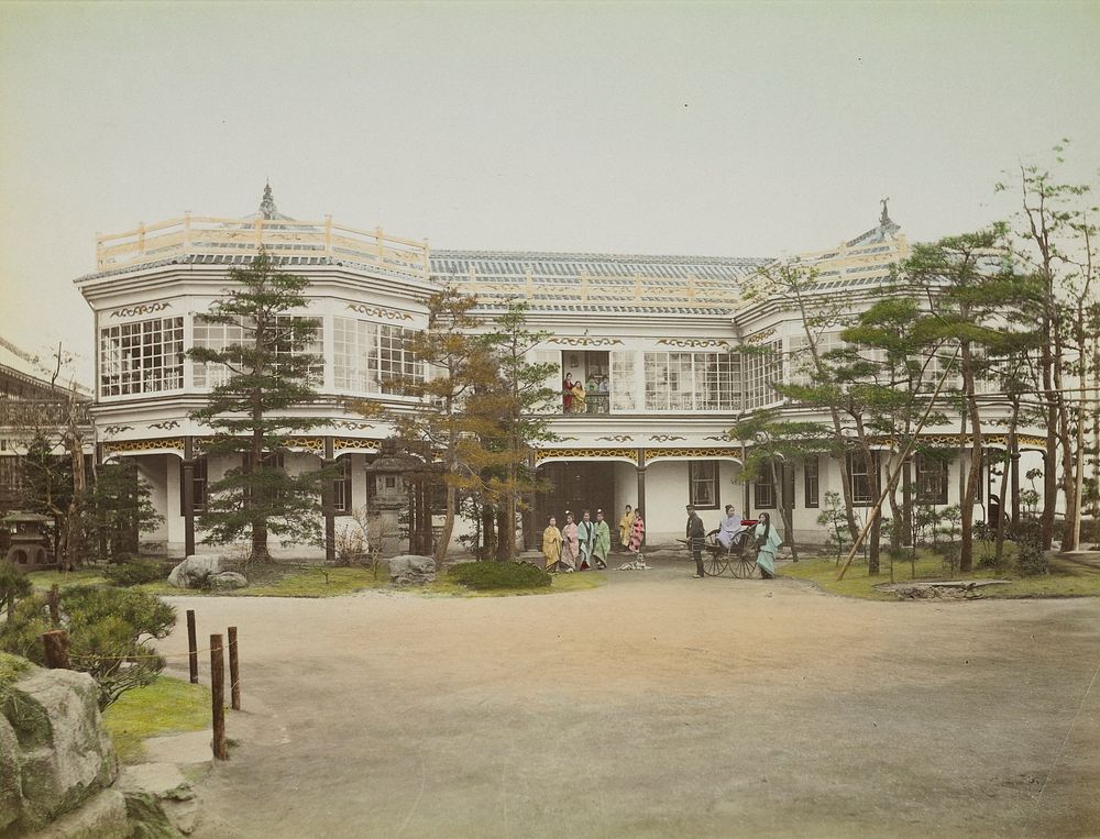large two-story building with blue tile roof; view across wide drive toward entrance of building; eight women, dog, and…