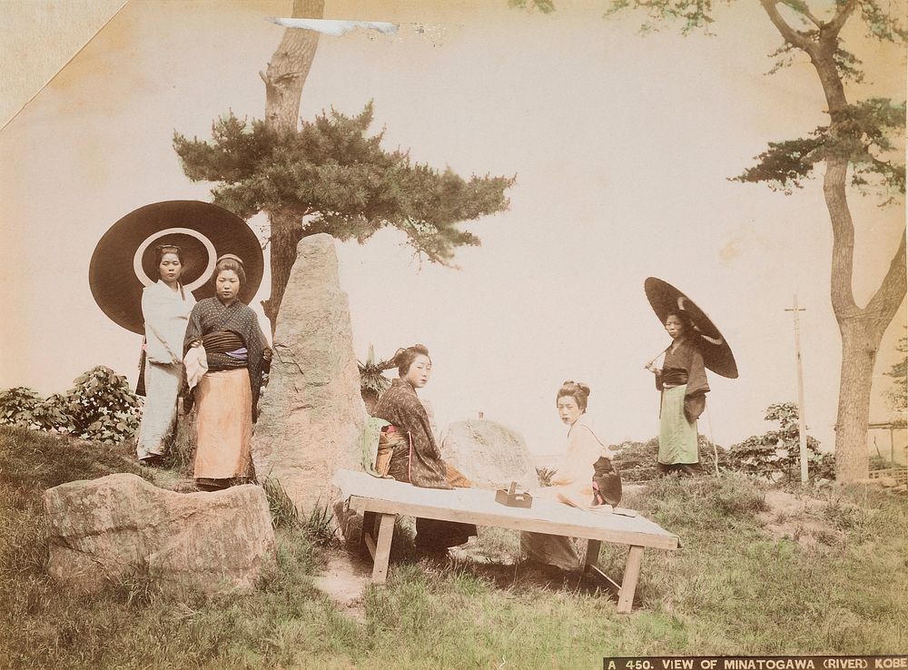 five women outdoors, wearing traditional Japanese garments; two women at center seated on a bench; two women at left stand…