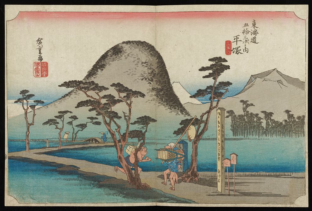 winding, narrow road crossing over calm waters; two male travelers struggle with luggage near signs at mouth of road; other…