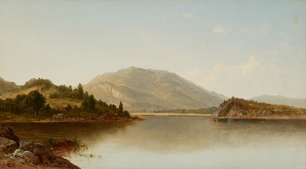 view over calm lake with mountain in background; green landforms with trees at left and right; rocks and grass in LLC; a few…