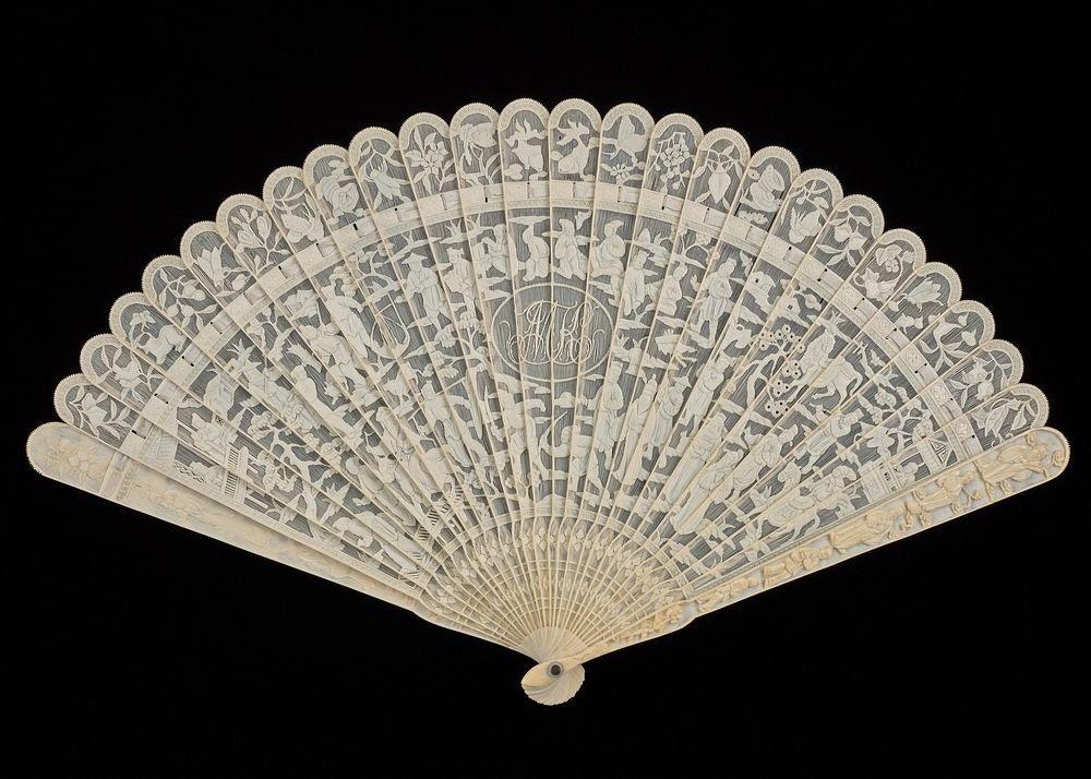 folding fan of ivory with cream colored ribbon at top of ribs; lacy openwork design; three cartouches with carved ladies in…