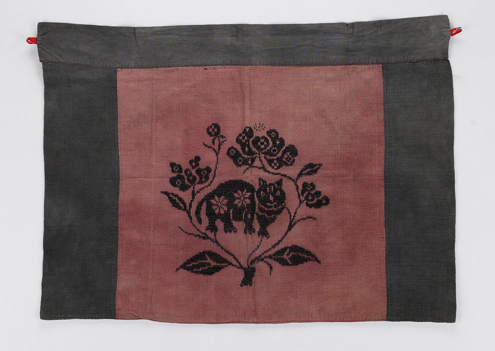 cat and foliage embroidered in black on dark pink ground; top and sides of apron bordered with grey fabric; there is a small…