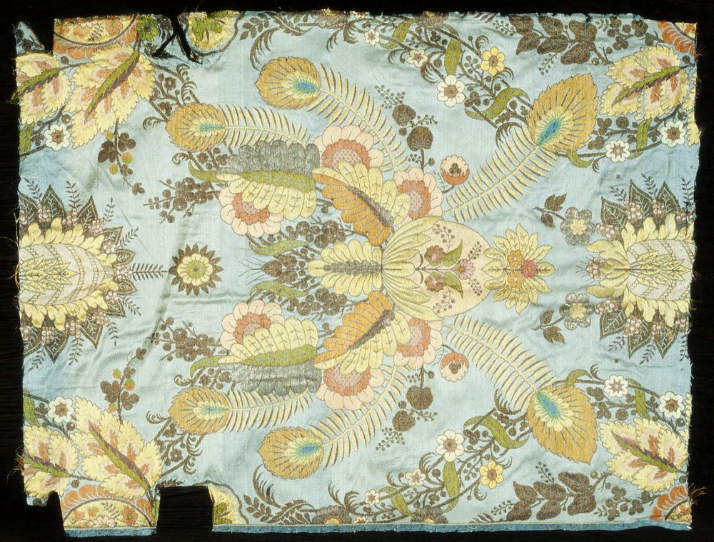 from a chair back upholstery; floral design with peacock feathers in peach, reds, green on gray-blue ground; patterned silk.…