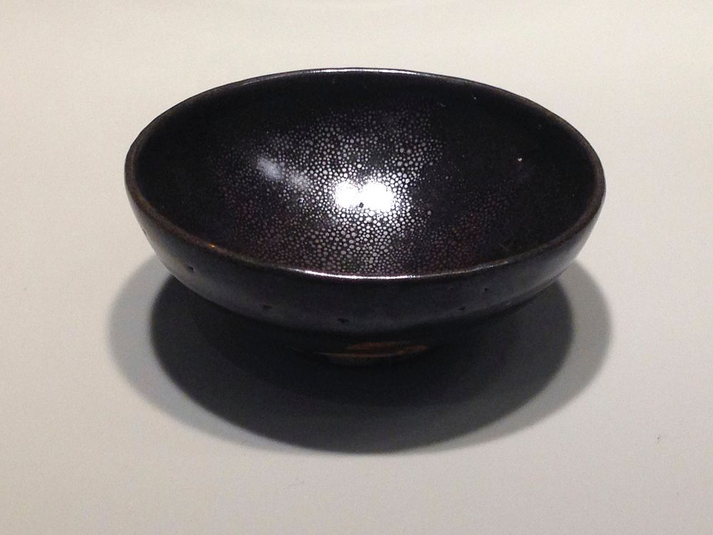 blackware, oil-spot glaze; small foot, straight lip; 2 layers of dark brown glaze, with silvery spotting on interior;…