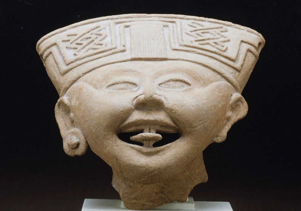 Smiling Face, ceramic, fragment of a larger figure, H. 5 in., W.7 in. Hollow head with open mouth and protruding tongue.…