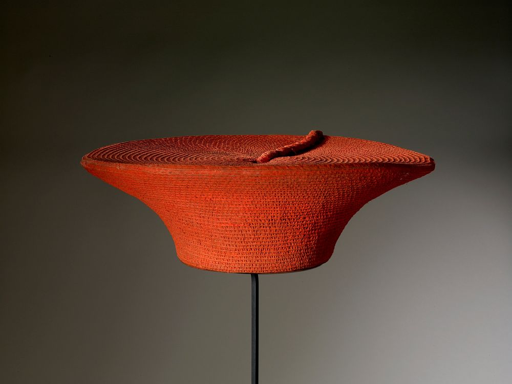 wide circular flat top with woven plait to one side; painted with red pigment; handle with latex gloves, pigment contains…