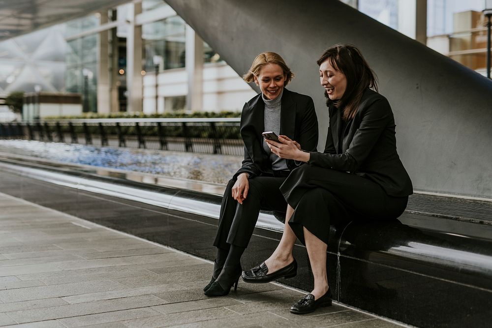 Businesswomen holding smartphone, laughing together