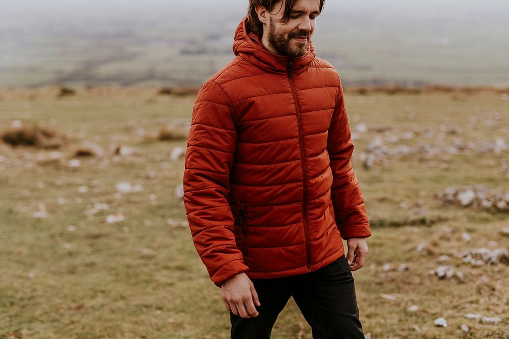 Man wearing orange puffer jacket, walking on hill