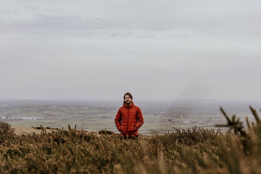 Man in orange puffer jacket, standing on hill