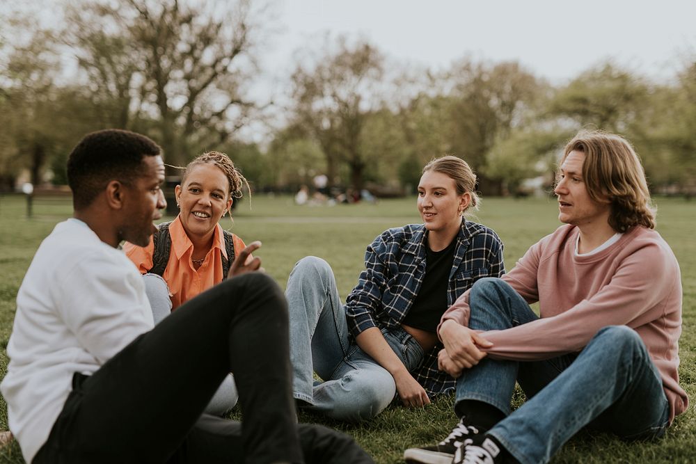 Cheerful diverse friends hanging out, sitting in a park