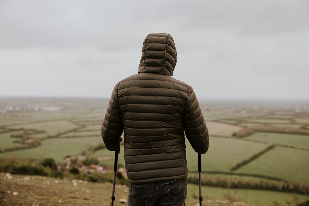 Man wearing jacket, holding hiking pole, rear view