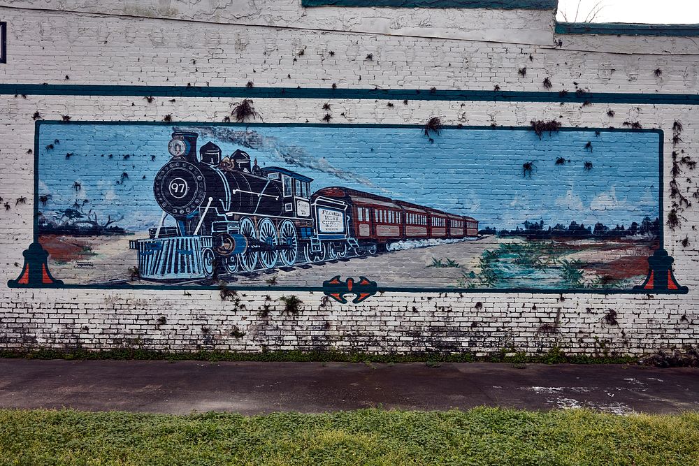                         A weathered mural, fittingly on a wall across from the train depot, showing an old-time steam…