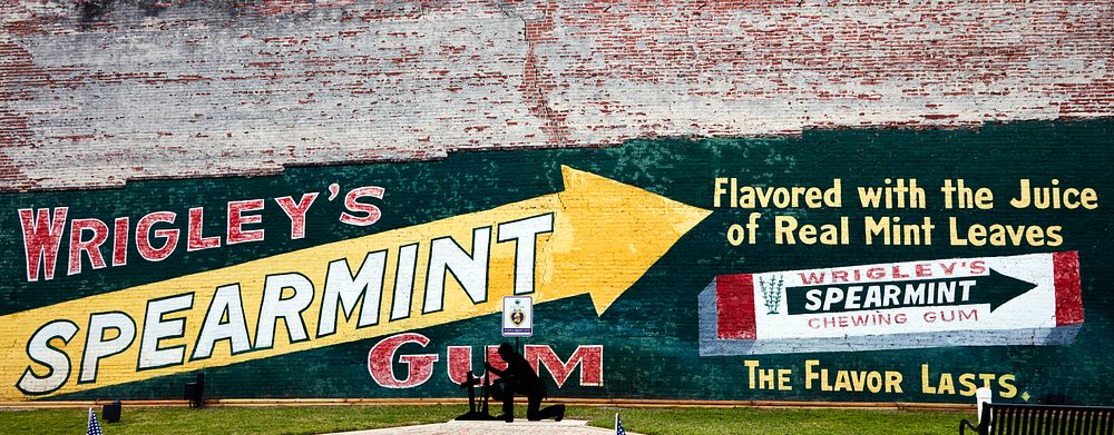                         An old Wrigley's Spearmint Gum advertising mural dwarfs a small war memorial in a park in Trenton, a…