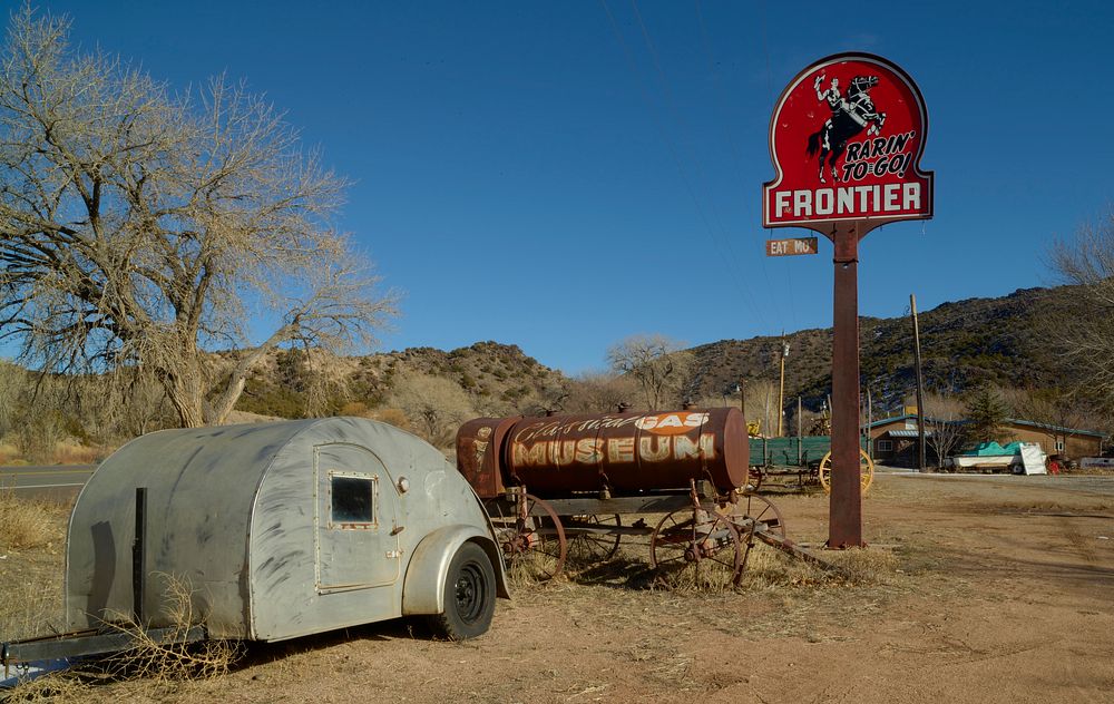                         An old camper stands beneath a Frontier Gasoline station sign at a nostalgic roadside attraction…