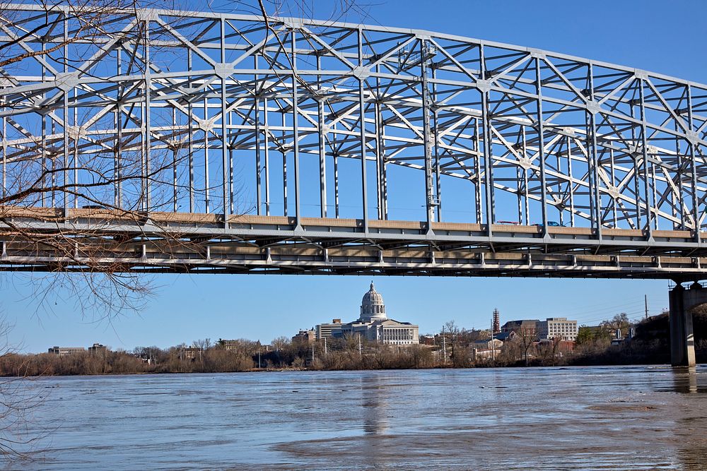                         The Missouri River and a pedestrian bridge over it, and, under it, a distant view of the Missouri…
