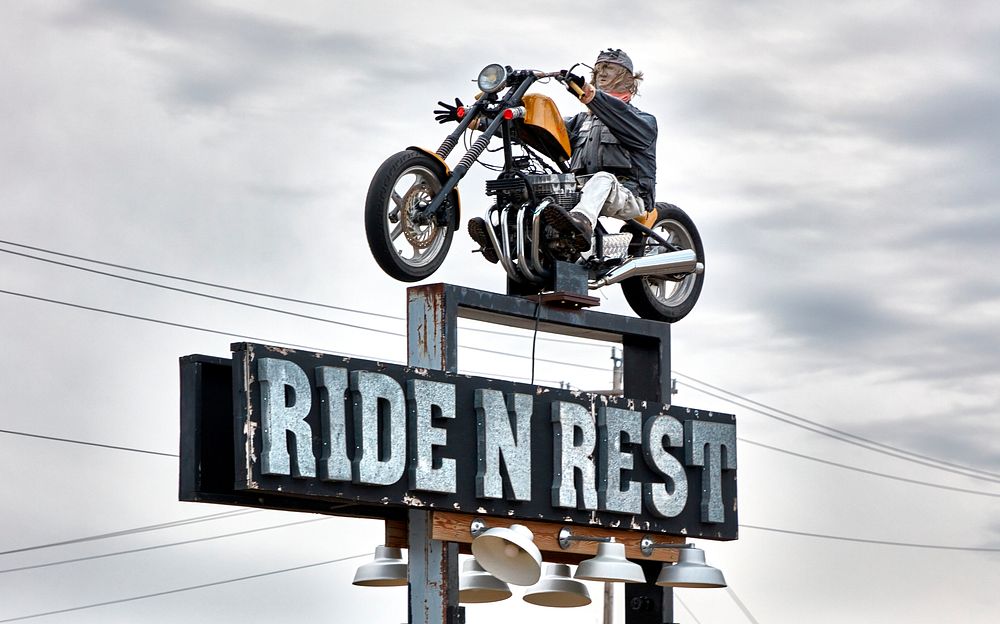                         Sign featuring a motorcyclist, hoping to attract guests to the Ride N Rest tourist cabins outside…