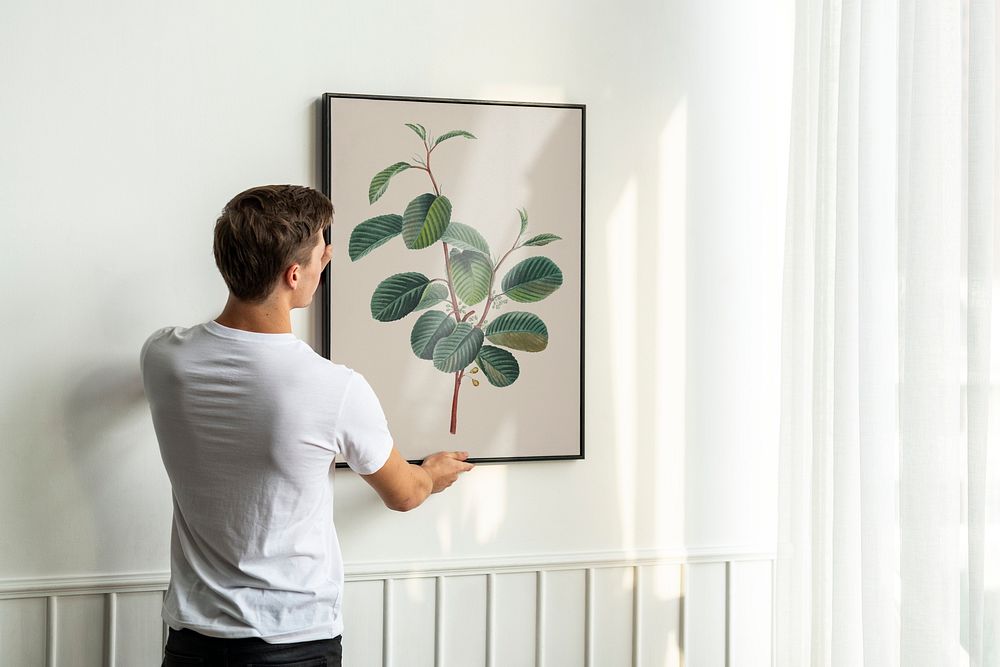 Vintage leaf painting frame psd being hung by a young man on a white minimal wall