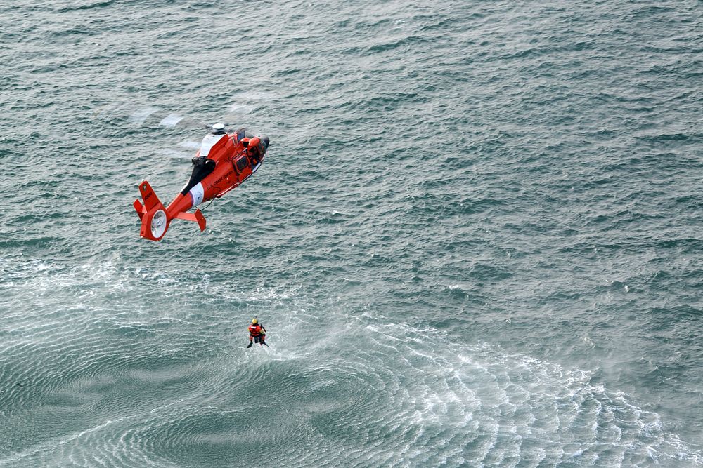 A U.S. Coast Guard aviation survival technician, rescue swimmer, is hoisted out of the water by the crew of MH-65 Dolphin…