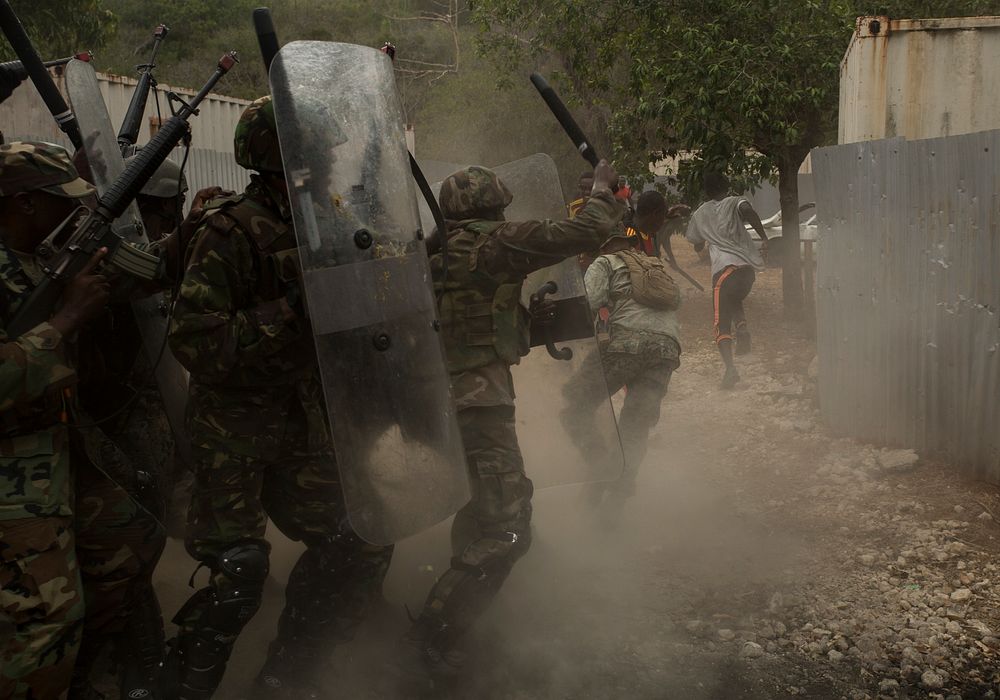 Service members from several different partner nations fend off role players acting as rioting villagers as part of crowd…