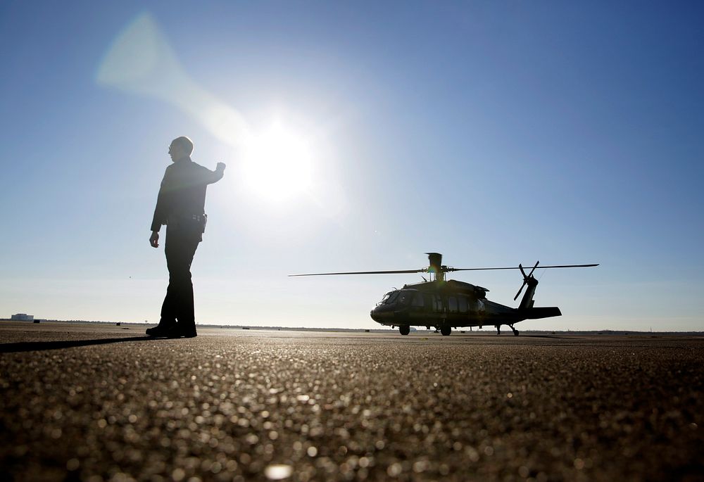 A ground support officer signals for a U.S. Customs and Border Protection Black Hawk helicopter to hold in place at…