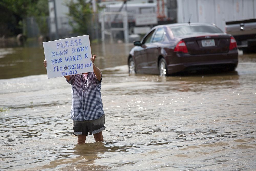 A resident holds a sign warning passersby to slow down to reduce wakes that exacerbate flooded streets in a suburb of…