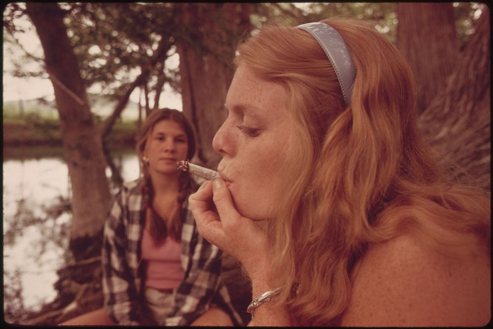 One Girl Smokes Pot While Her Friend Watches During an Outing in Cedar Woods near Leakey, Texas. Original public domain…