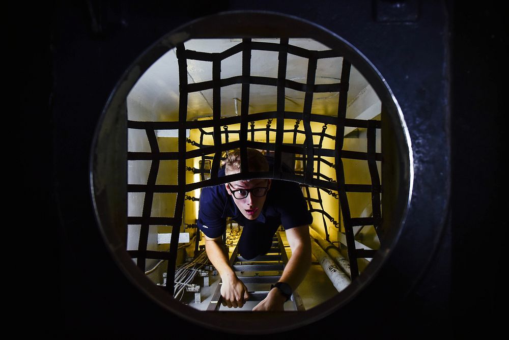 U.S. Navy Machinist’s Mate Fireman Shane Brooks climbs up a ladder leading from a shaft-alley aboard the aircraft carrier…