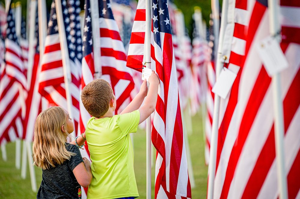 Children read a dedication card on a flag at the Field of Honor at Greenville Town Common, Greenville, date unknown, photo…