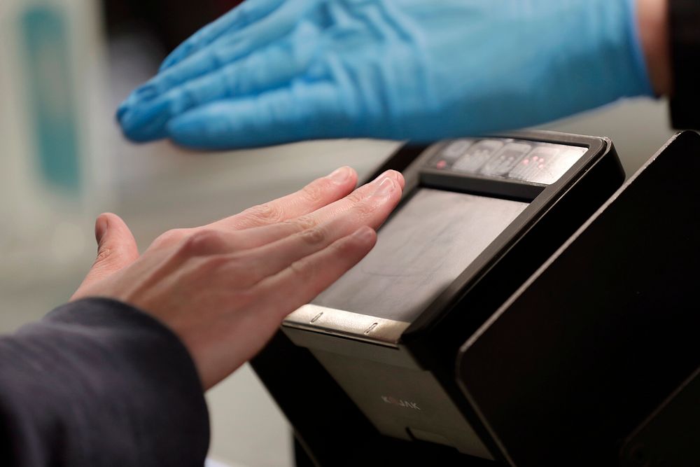 An arriving passenger places his hand, left, on a device to take his fingerprints as Officers with U.S. Customs and Border…
