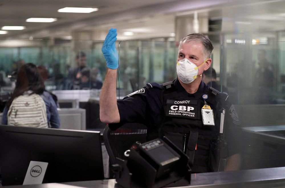 An officer with U.S. Customs and Border Protection Office of Field Operations gestures for arriving international travelers…