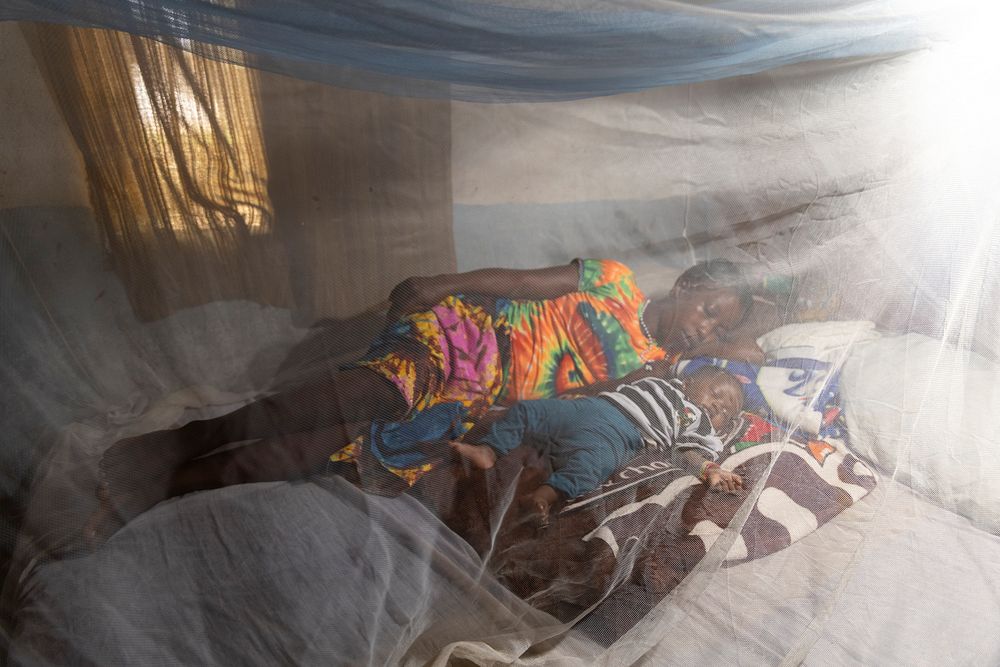 Mother and child rest under a mosquito net. Original public domain image from Flickr