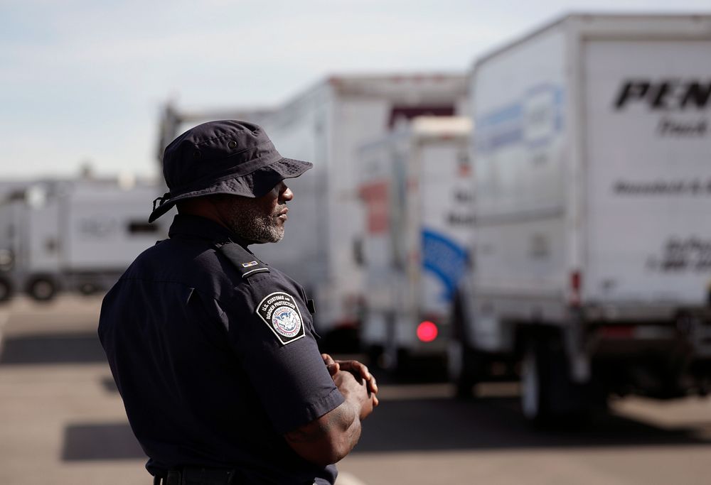 An officer with U.S. Customs and Border Protection Office of Field Operations observes a line of trucks awaiting their turn…