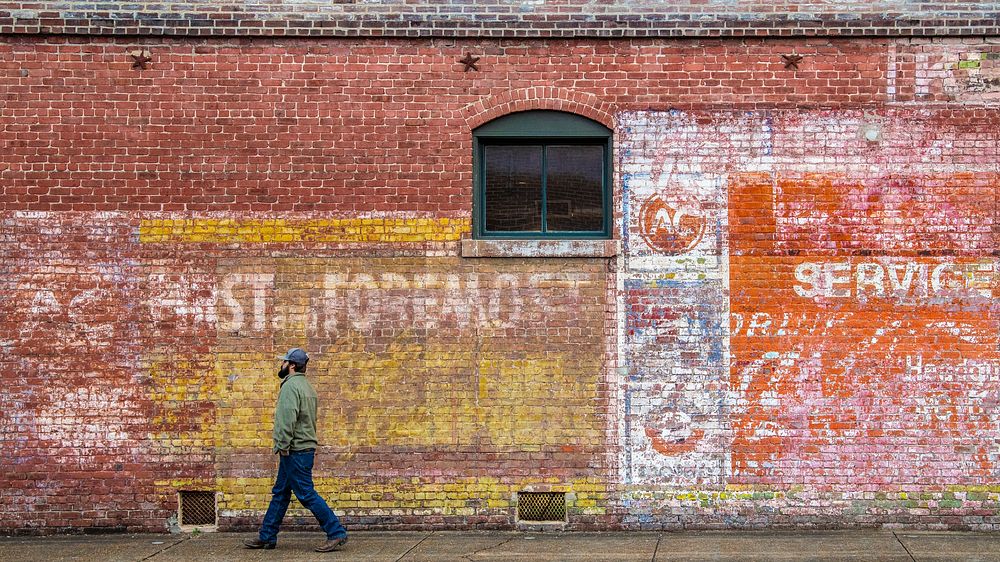 A man walks past a faded wall signage in Central Historic District and Railroad Historic District of Greenwood, MS, on…