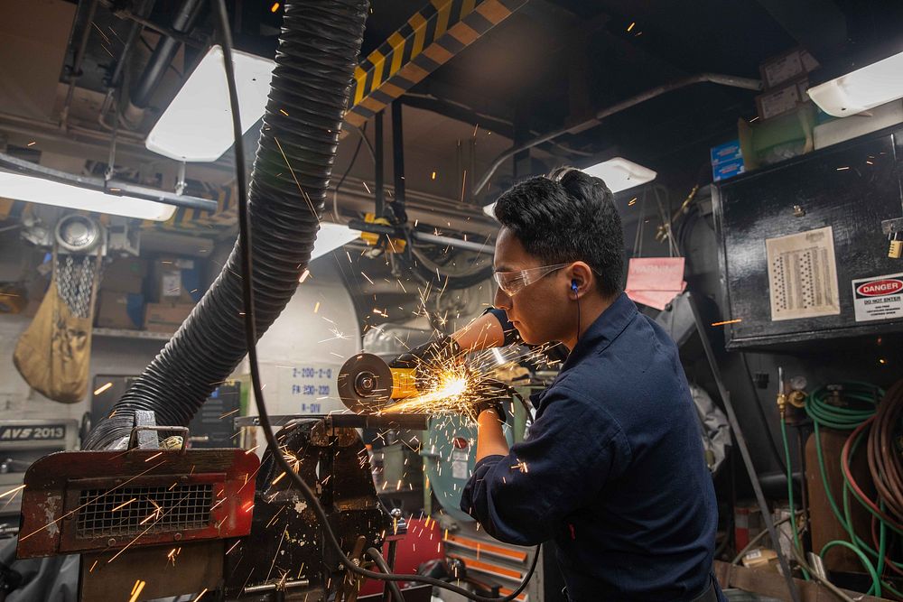 Hull Technician 3rd Class Kevin Agustin grinds metal in the general workshop aboard the Arleigh Burke-class guided-missile…