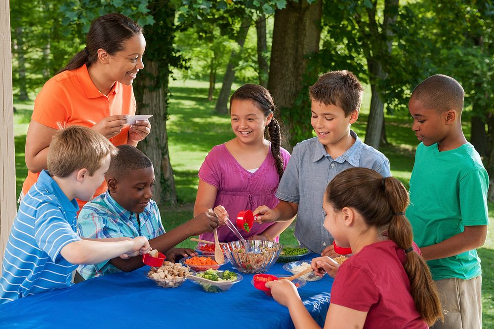 Children participating in nutrition education at a summer meals site. Teacher and children making pasta salad. Original…