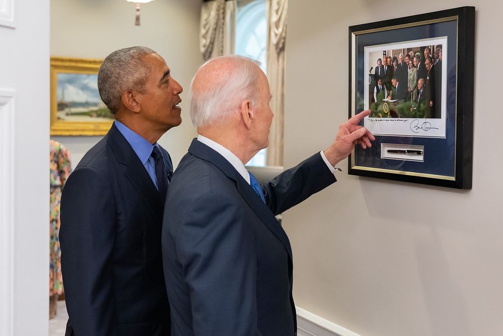 President Joe Biden and former President Barack Obama look at a framed photo and commemorative pen from the 2010 signing…