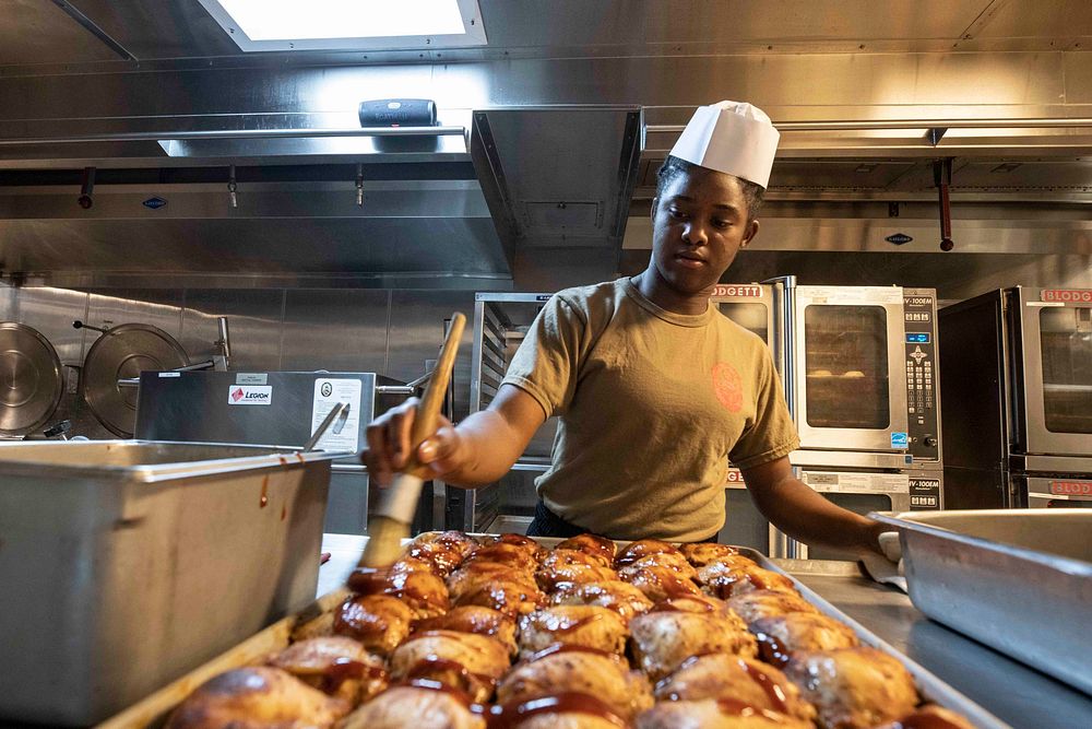 RED SEA (June 14, 2022) Culinary Specialist Seaman Taylen Turner, from Monroe, Louisiana, coats chicken in barbecue sauce…