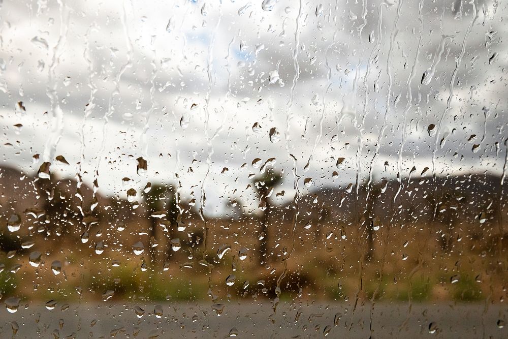 Rain on car windowAlt text: Raindrops are scattered across a car window. Out of focus and through the glass lies the desert…