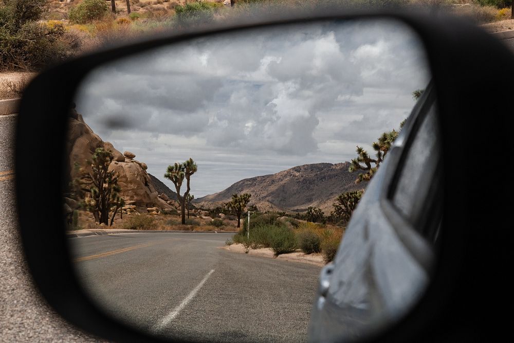 Storm clouds in mirror viewAlt text: A car's side view mirror reflects the road behind it and the approaching storm…
