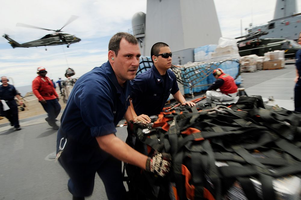 U.S. Navy Hull Technician 2nd Class Seneca Jernigan, left, and Yeoman 3rd Class Steven Tai move pallets of humanitarian…