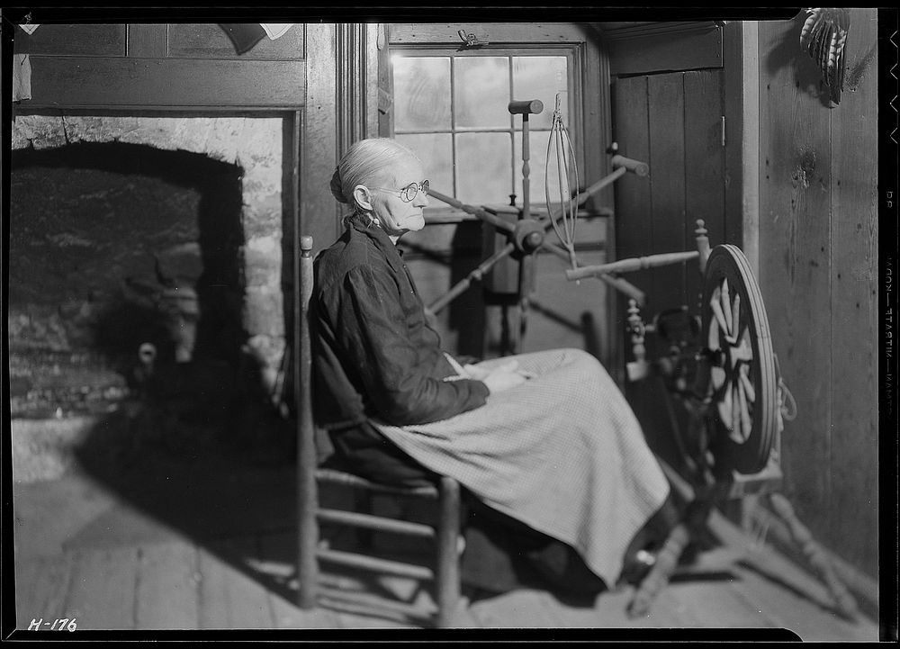 Another view of Mrs. Jacob Stooksbury, seated before a spinning wheel in her home. The creel in the background is used for…