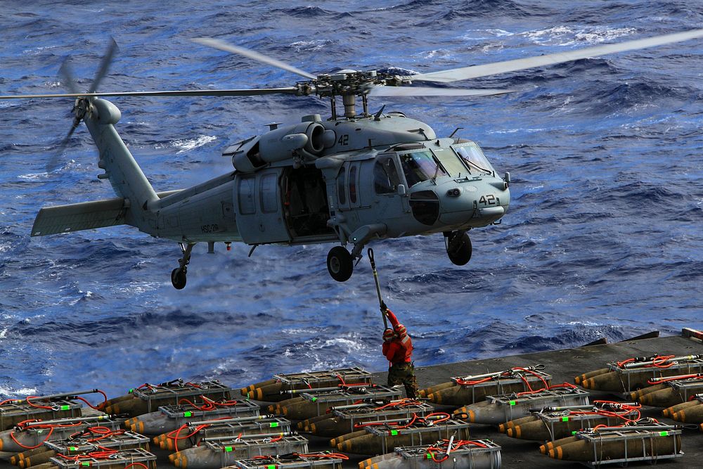 U.S. Sailors aboard the aircraft carrier USS Enterprise (CVN 65) attach pallets of ammunition to an MH-60S Knighthawk…