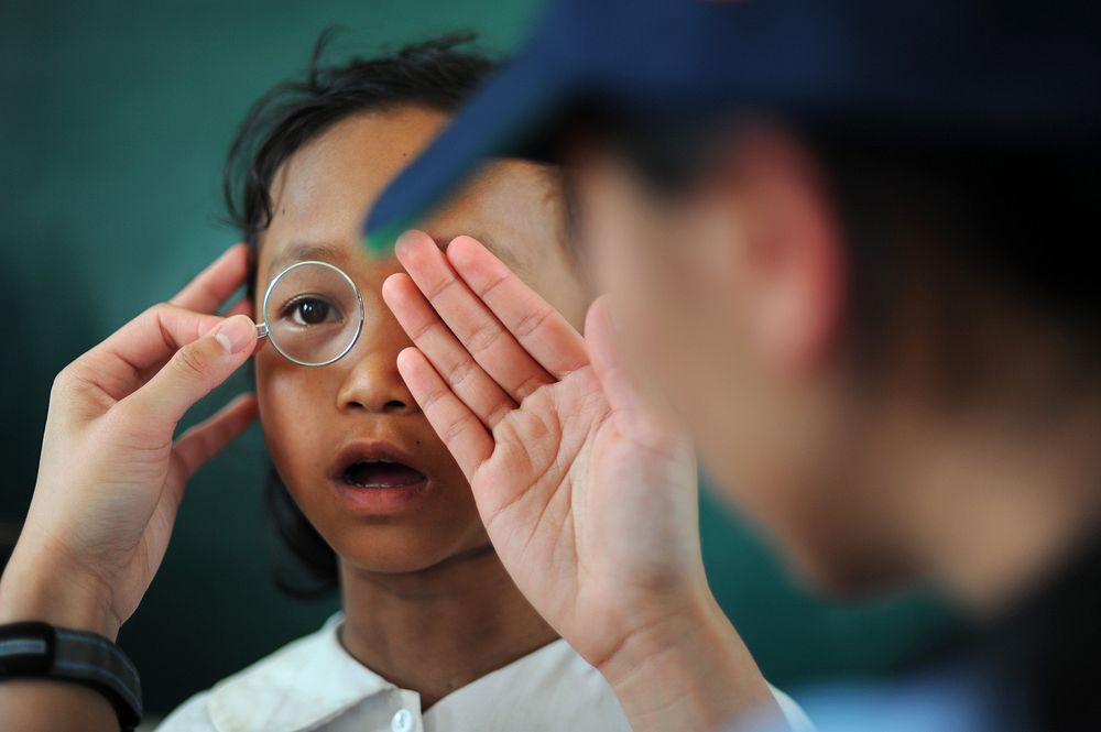A patient looks through a lens to determine what prescription she needs for eyeglasses during Operation Pacific Angel 2013…
