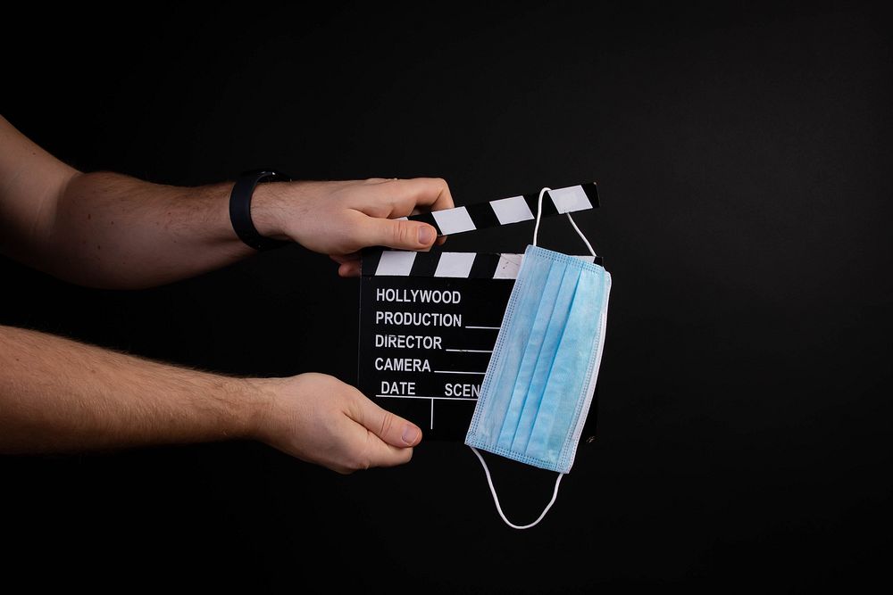 Hand holding movie clapper and medical face mask on black background   