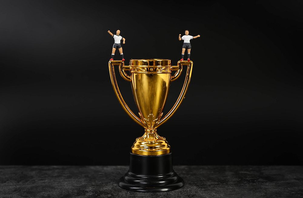 Miniature football players standing on golden trophy   