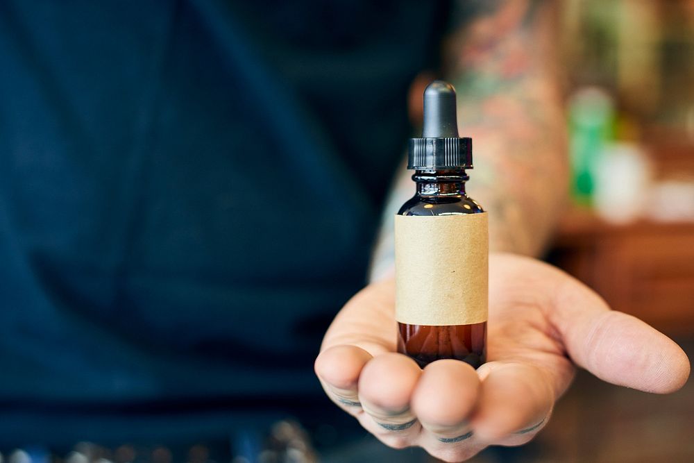 Close up of a bottle of homemade beard oil in the hand of a man.