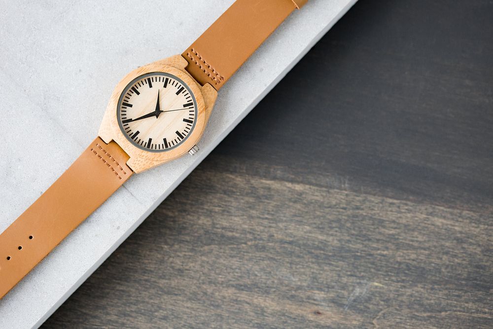 Wooden watch with leather wrist band and black hands.