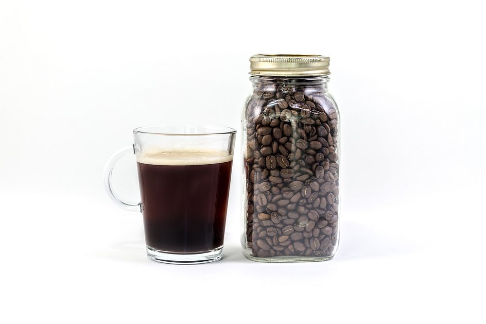 Clear glass mug of coffee next to a jar of roasted coffee beans.