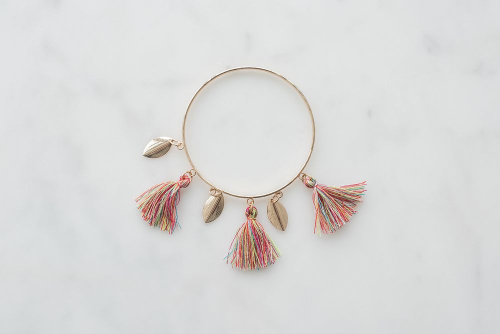 Gold bangle bracelet with gold metal feathers and multicolor tassels.