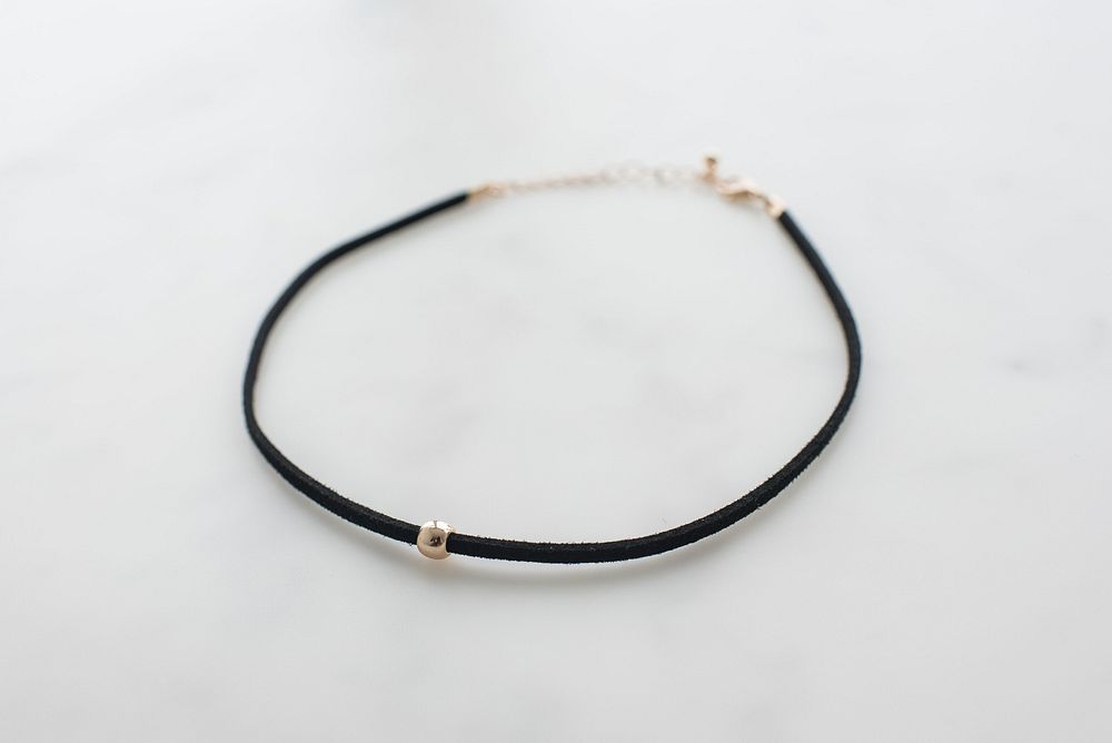 Product photo of black choker necklace with gold bead.